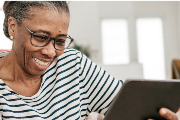 Retired woman wearing pin-striped long sleeve shirt looking at her finances on a tablet in the comfort of her home