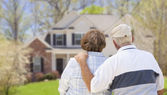 Happy Senior Couple From Behind Looking at Front of House. Senior couple stands with arms around one another looking at a house