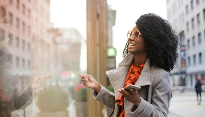 Young-Woman-Reflection-Slideshow Young woman smiling at her reflection in a building's window on a major city street
