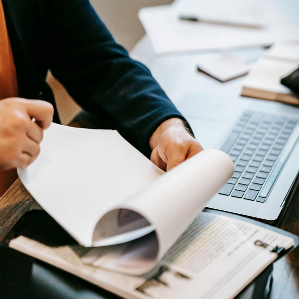 A graduate student whose research is supported by a fellowship flips through papers at a desk with more papers and a laptop