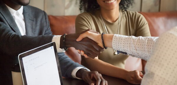 Happy young african american couple making deal handshaking caucasian insurance broker in cafe, black satisfied customer and realtor or sales person shaking hands at meeting in office with laptop