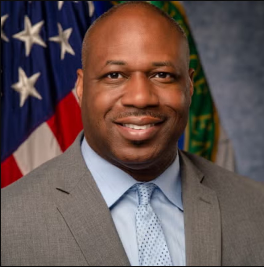 Dr. McKoy, a middle-aged man wearing a gray suit with light blue shirt and tie, smiles for a posed photo